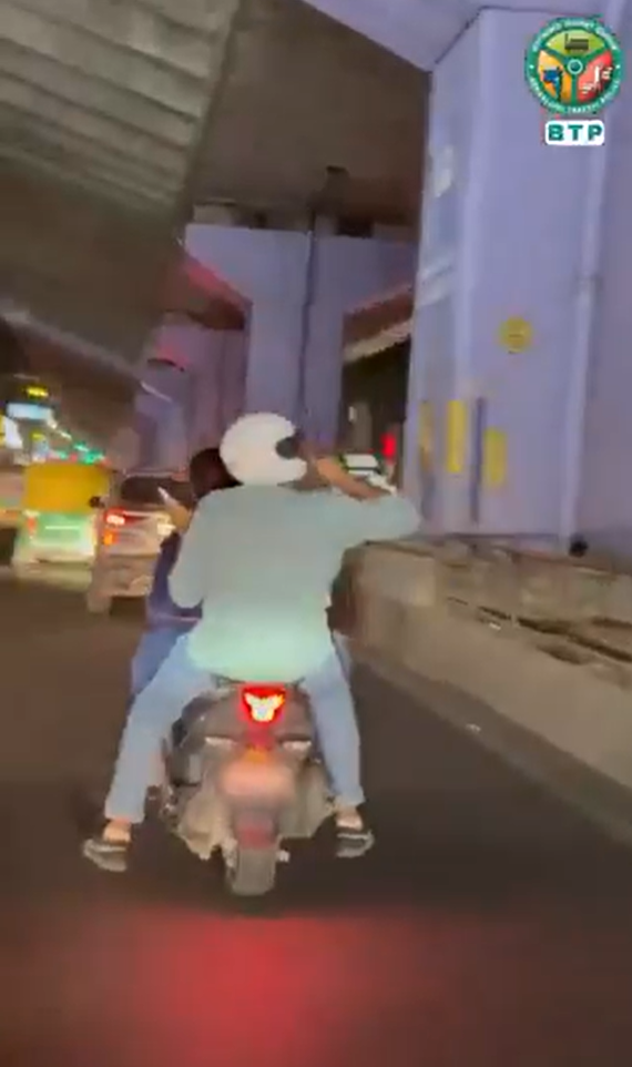 ಮೇಲ್ಸೇತುವೆಯ ಕೆಳಗಿನ ರಸ್ತೆಯಲ್ಲಿ ಸ್ಕೂಟರ್‌ನಲ್ಲಿ ಸಾಗುತ್ತಿರುವ ಇಬ್ಬರು ಸವಾರರ ಹಿಂಬದಿಯ ದೃಶ್ಯ; ಬೆಂಗಳೂರು ಸಂಚಾರ ಪೊಲೀಸ್ ಲಾಂಛನ